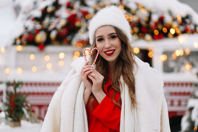 A beautiful young woman with red lips in a warm hat stands by decorated christmas van on the street