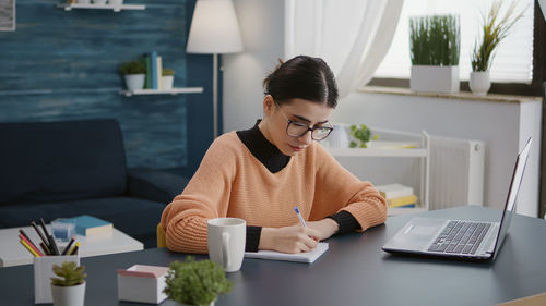 Side view of young woman using laptop at home