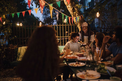 Smiling young woman showing mobile phone to female friends at table during dinner party