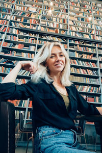 Portrait of smiling woman sitting against bookshelf