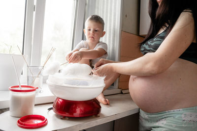 Midsection of pregnant mother and son making cotton candies at home