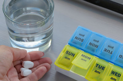 Close-up of woman hand holding pills by box and glass of water