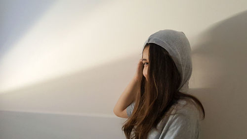 Woman wearing hooded shirt while standing by wall