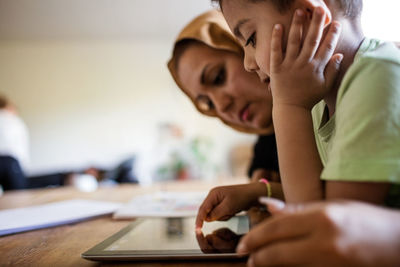 Side view of mother and son using digital tablet while studying at home