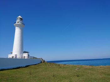 Lighthouse by sea against clear blue sky