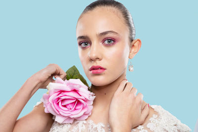 Portrait of young woman holding rose against blue background
