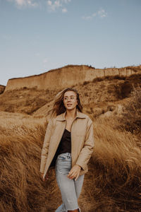 Portrait of smiling young woman standing on land against sky