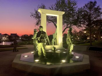 Illuminated statue in park against sky at sunset