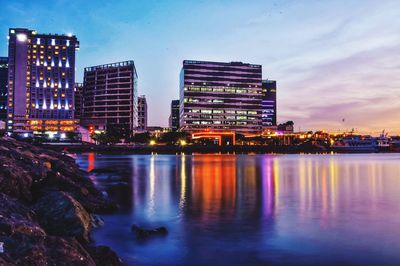 Illuminated buildings by river against sky in city at night