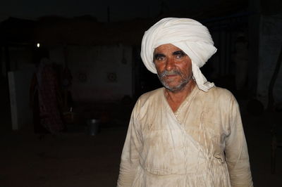 Portrait of man wearing traditional clothing while standing against black background