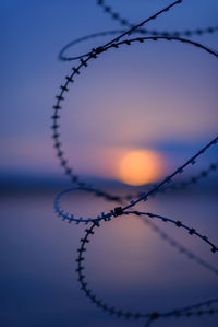 Close-up of barbed wire against sky during sunset