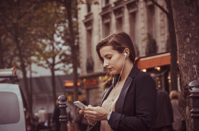 Young woman using mobile phone standing against building