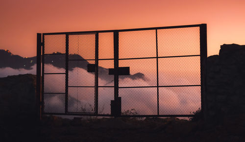 Silhouette fence against orange sky