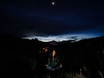 Man sitting on mountain against sky at night