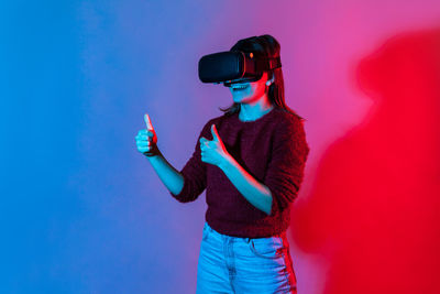 Woman wearing virtual reality simulator while standing against colored background