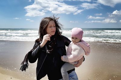 Mother carrying daughter at beach against blue sky