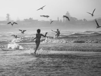 Girl running behind birds flying over sea