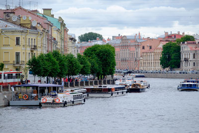 Boats in river by buildings in city against sky