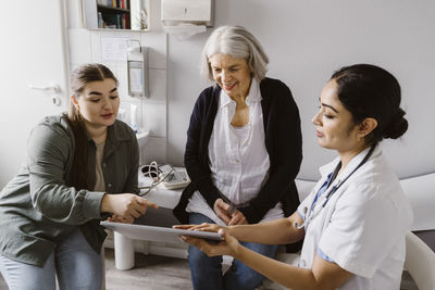 Doctor discussing with senior woman and daughter over tablet pc in clinic