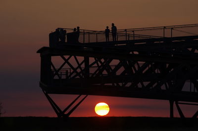 Silhouette people on bridge against sky during sunset