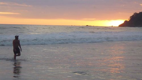 Man walking on beach against sky during sunset