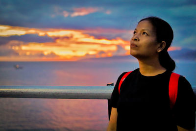 Boy looking at sea against sky during sunset