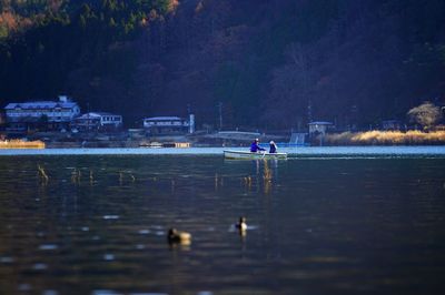 People sailing on lake against trees