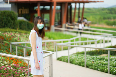 Side view of young woman standing against railing