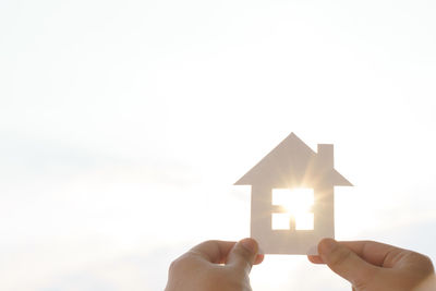 Cropped hands holding model home against sunlight