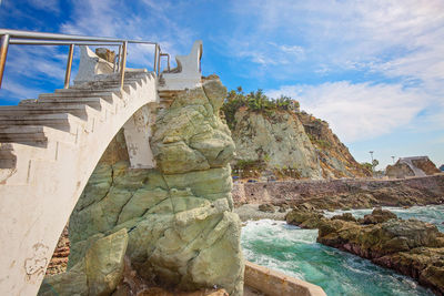 Bridge over rocks against cloudy sky