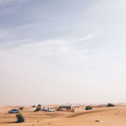 Vehicles on arid landscape against sky on sunny day