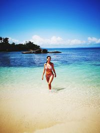 Woman wearing bikini while walking at beach against sky