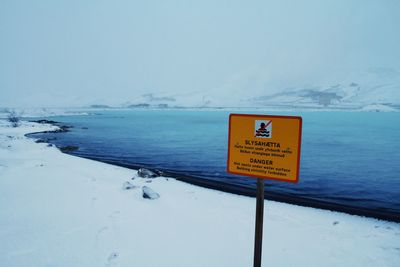 Information sign on snow covered shore against sky