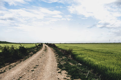 Dirt road amidst field against sky