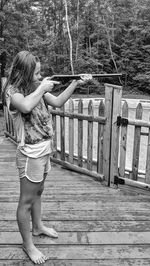 Side view of girl aiming with gun while standing on wood