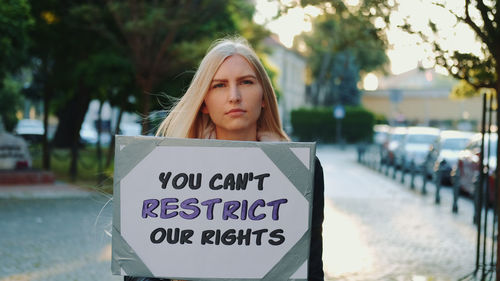 Portrait of young woman standing against sign