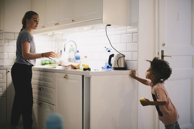 Boy looking at mother working in illuminated kitchen