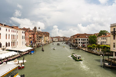 Boats in grand canal amidst buildings against cloudy sky