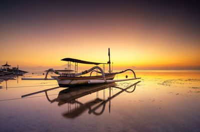 Fishing boat moored at shore against sky during sunset