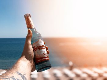 Close-up of hand holding bottle against sea against sky