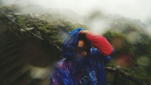 Close-up of woman wearing raincoat while standing on staircase during rainy season