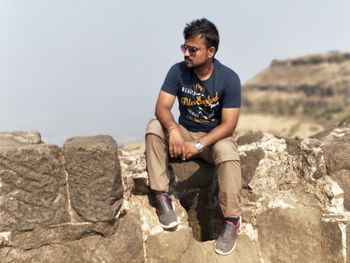 Young man standing on rock against clear sky