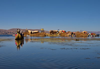 Uros man transporting tourists on a reed boat next to his floating island on lake titicaca