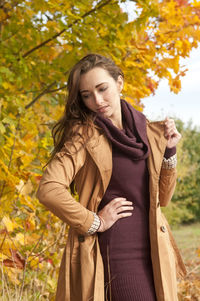 Woman wearing coat standing against trees in park during autumn