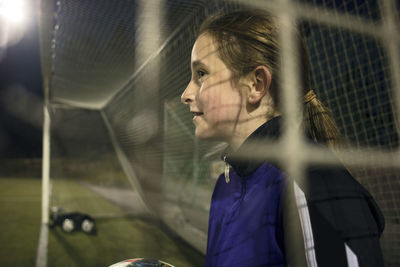Side view of girl with soccer ball seen through goal post net