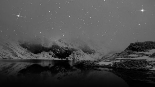 Scenic view of sea and mountains against sky at night