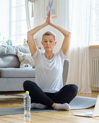 Senior woman in lotus position, online training in living room. emotional health, meditation.