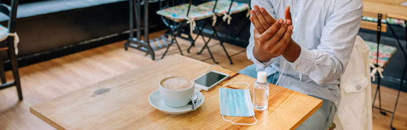 Midsection of man using hand sanitizer at cafe