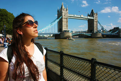 Young woman with sunglasses on bridge against sky