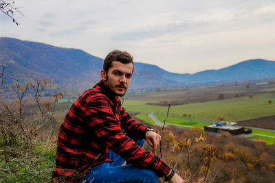 Portrait of man sitting on field against sky